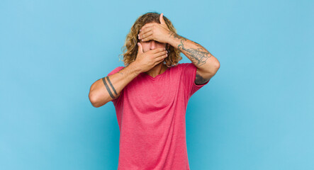 blonde man covering face with both hands saying no to the camera! refusing pictures or forbidding...