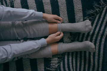 Hands unrecognizable girl puts on some socks on a cold day to spend at home. Winter Photography. Cozy Home Concept.