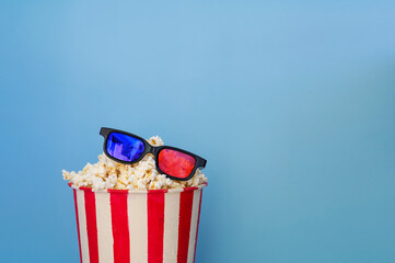 A bucket full of popcorn on a blue background and 3D glasses.