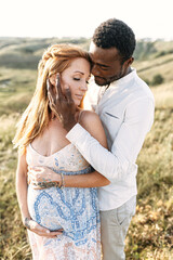 A portrait of multiethnic couple in love, they are looking forward a baby. A handsome black guy is hugging his beautiful pregnant wife and touching her face tenderly