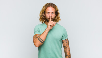 blonde man looking serious and cross with finger pressed to lips demanding silence or quiet,...