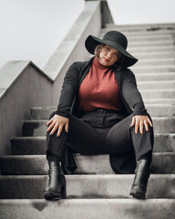 Brunette woman in hat sitting on the stairs of building in city