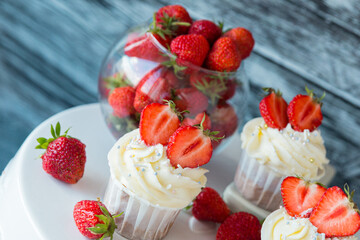 cupcake in the center with white cream decorated with ripe strawberries on a gray blue background and scattered strawberries.