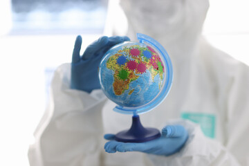 Hands of doctor in protective suit are holding globe. Spread of coronavirus in the world concept