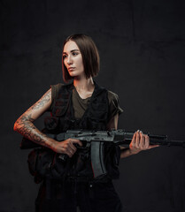 Holding assault rifle martial woman in black armour with short haircut poses in dark background.