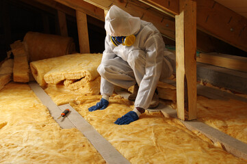 Worker thermally insulating house attic with glass wool