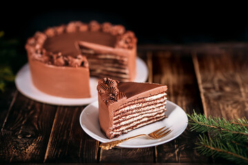 Chocolate cake on a white plate. Against the background of a branch of a Christmas tree. Wooden table with a beautiful pattern. Traditional sweets for birthday and other holidays