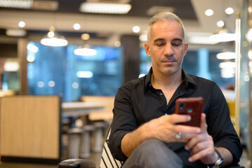 Portrait of man sitting in coffee shop using mobile phone