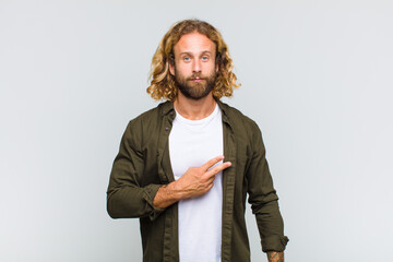blonde man feeling happy, positive and successful, with hand making v shape over chest, showing...