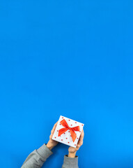 Christmas photo on a blue background, a man holding a beautiful present with a red ribbon, template with copy space