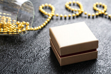Gift box on a black background near a glass with gold beads.