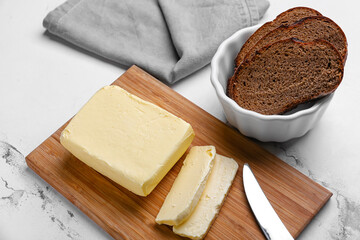 Butter, knife and bowl with bread on wooden board