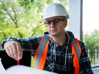 A male engineer in a white helmet looks at a sketch of a building construction plan. Contractors...