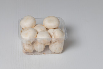 White champignon mushrooms in a transparent bowl are isolated on a white table.