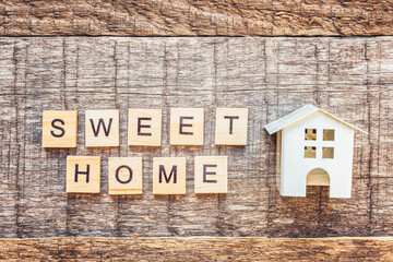 Miniature toy house with inscription SWEET HOME letters word on wooden background. Mortgage property insurance dream home concept. Flat lay top view, copy space