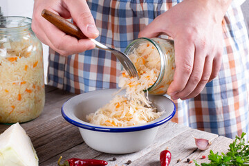 Man putting homemade sauerkraut from jar into bowl at wooden table - obrazy, fototapety, plakaty