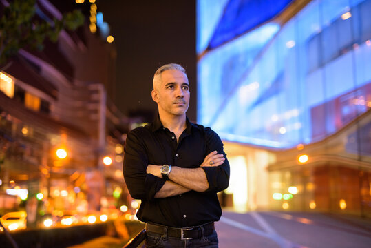 Portrait of attractive man thinking at night on the streets arms crossed