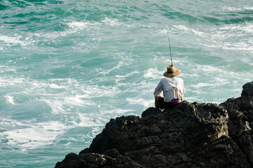Back view of man fishing in the ocean from rocks