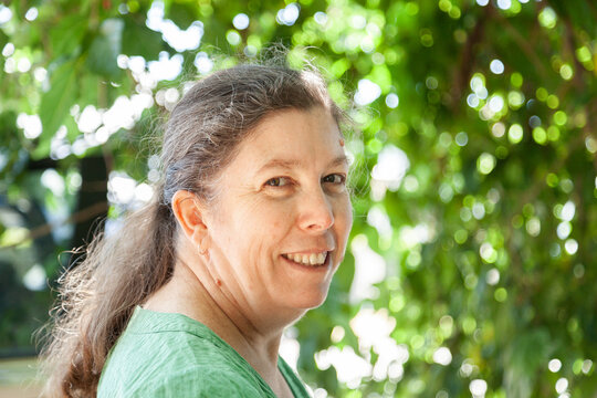 Portrait of a happy middle aged woman standing under green tree