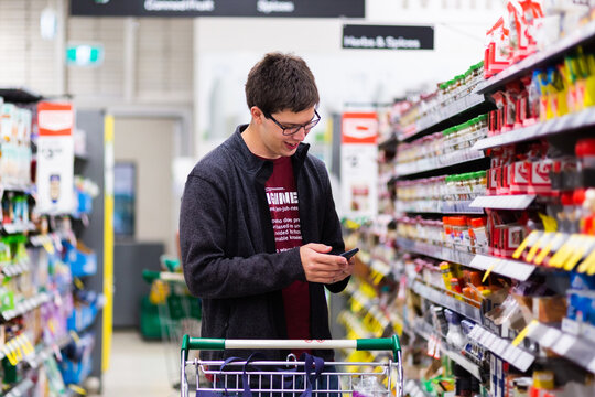 Young man in his 20s doing the family grocery shopping checking shopping list on his phone