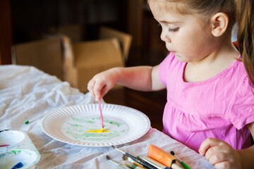 Little girl in pink painting on a paper plate