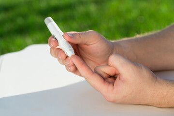 Medicine, diabetes, glycemia, healthcare and people concept - close up of a man's hands using a lancet on his finger to check blood glucose meter with copy space for text