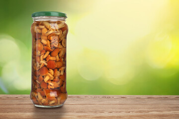 Jar of pickled mushrooms on wooden table against blurred background, space for text