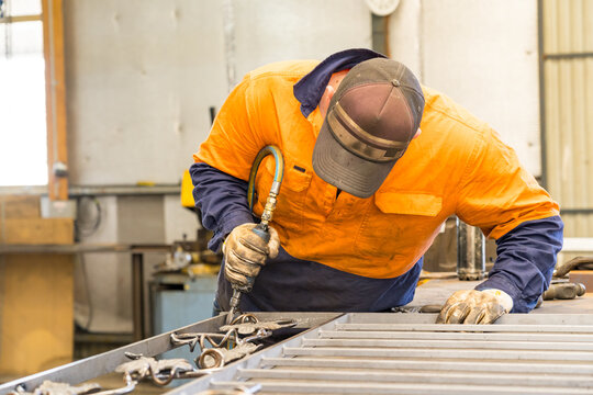 A tradesman wearing high vis clothing grinding steel on a workbench
