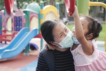 Fototapeta na wymiar Asian mother wearing a black shirt and a mask is teaching her daughter to play the ring bar in the playground on the weekend.