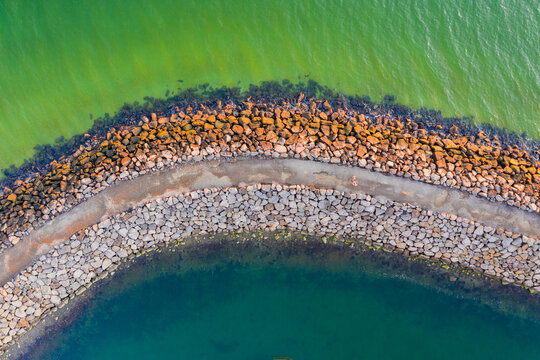 Looking straight down on a curved section of a breakwater with different coloured water on each side
