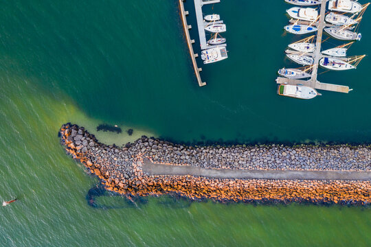Looking straight down on the end of a narrow rock breakwater shielding rows of yachts