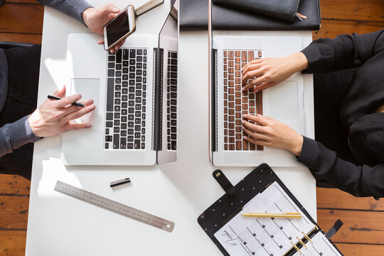 Overhead view of two people working on their laptop keyboards