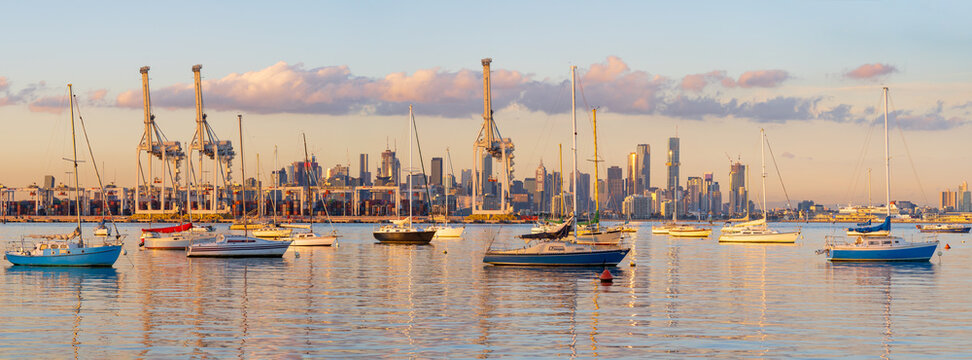 Yachts anchored on still bay in front of large gantry cranes at a cargo dock