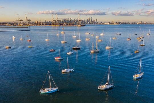Aerial view of yachts anchored on a calm bay with city skyline in the background