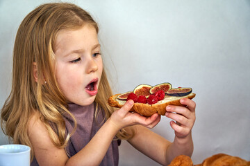 French breakfast sandwich with croissant and figs in the hands of a child girl. Toast with berries