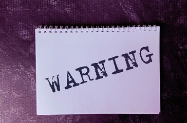 The word Warning on a white Notepad on a purple structural background.