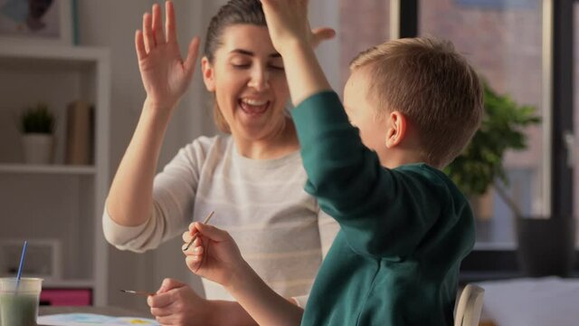 family, leisure and people concept - mother and little son with colors and paper drawing at home and making high five gesture