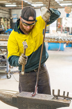 A smiling tradesman wearing high vis clothing hammering a steel rod on an anvil