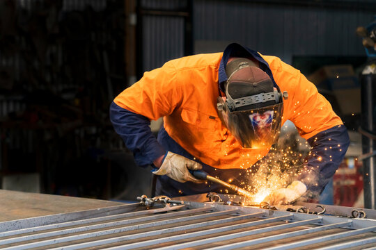 A tradesman wearing high vis clothing welding steel on a workbench