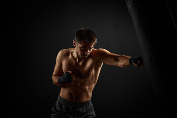 Fototapeta na wymiar Male boxer punching in boxing bag on black background