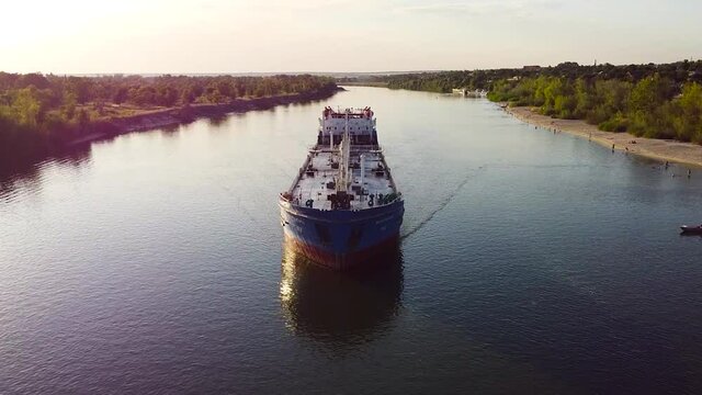 Top view of cargo ship sailing on Volga. Footage. Long boat for cargo transportation on river on background of beach with vacationers. Inland freight water transport in summer