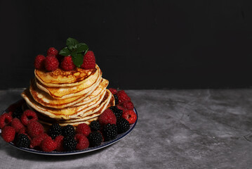 A pile of homemade pancakes on a plate with raspberries and blackberries on a dark background . The concept of homemade pastries. Copy space