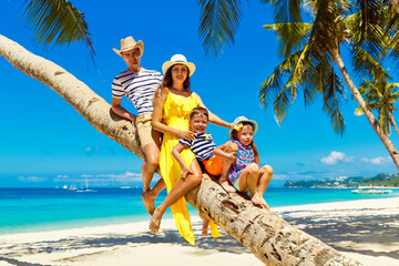 Young happy family-mom, dad, daughter and son having fun on a coconut tree on a sandy tropical beach. The concept of travel and family holidays. © frolova_elena