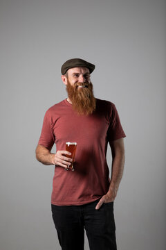 Trendy man with ginger beard and flat cap, holding a glass of beer