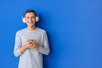 Young man with headphones and mobile phone on color background