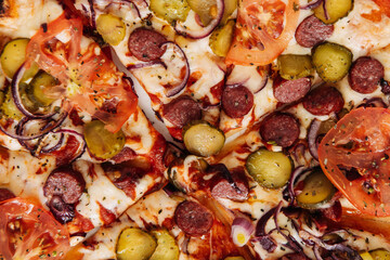 Pizza with pepperoni, pickled cucumbers and tomatoes on a light background close-up, top view