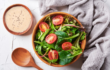 green salad from green leaves and cherry tomato in wooden bowl on white stone background. top view