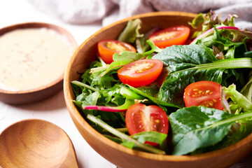 close up green salad from green leaves and cherry tomato in wooden bowl on white stone background