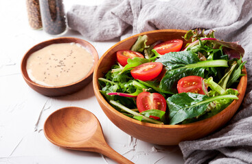 green salad from green leaves and cherry tomato in wooden bowl on white stone background