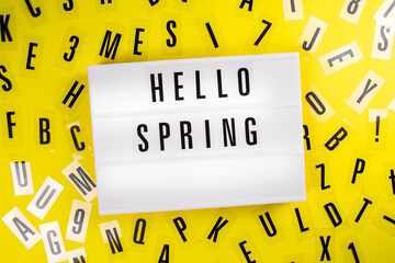 Hello Spring text on lightbox on scattered letters background of plastic alphabet. Springtime postcard design with positive saying. holiday season slogan. concept